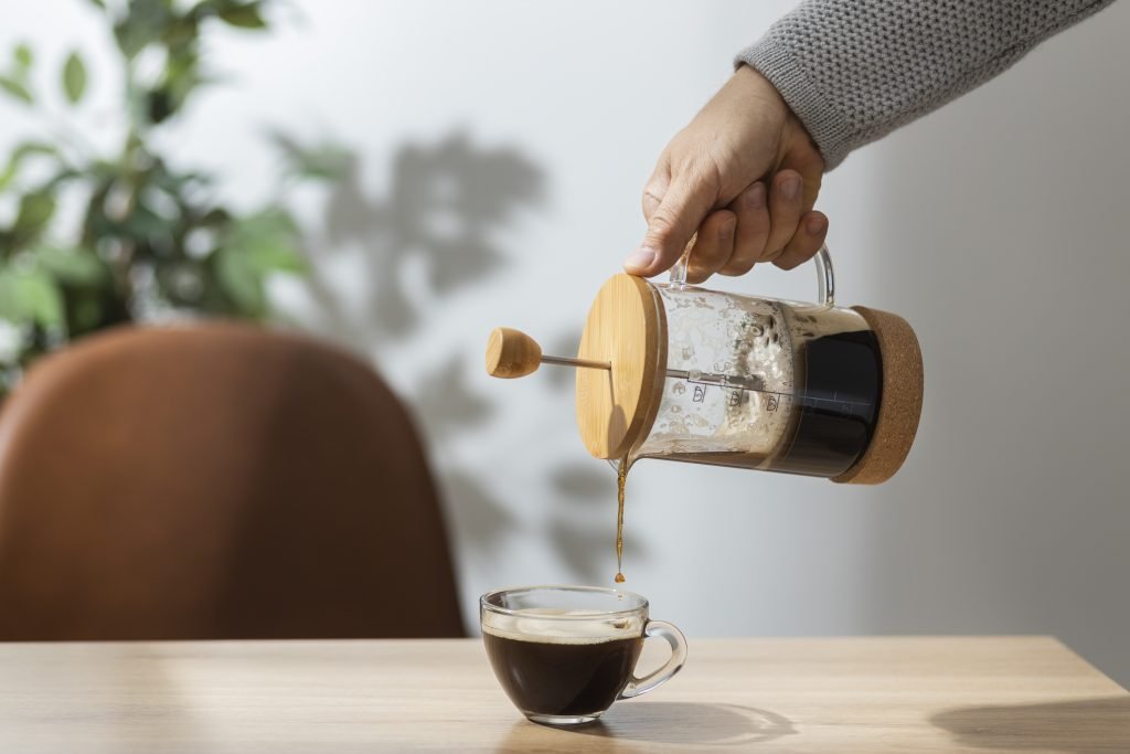 Vista lateral de uma pessoa servindo uma xícara de café com uma prensa francesa. Imagem de Freepik.